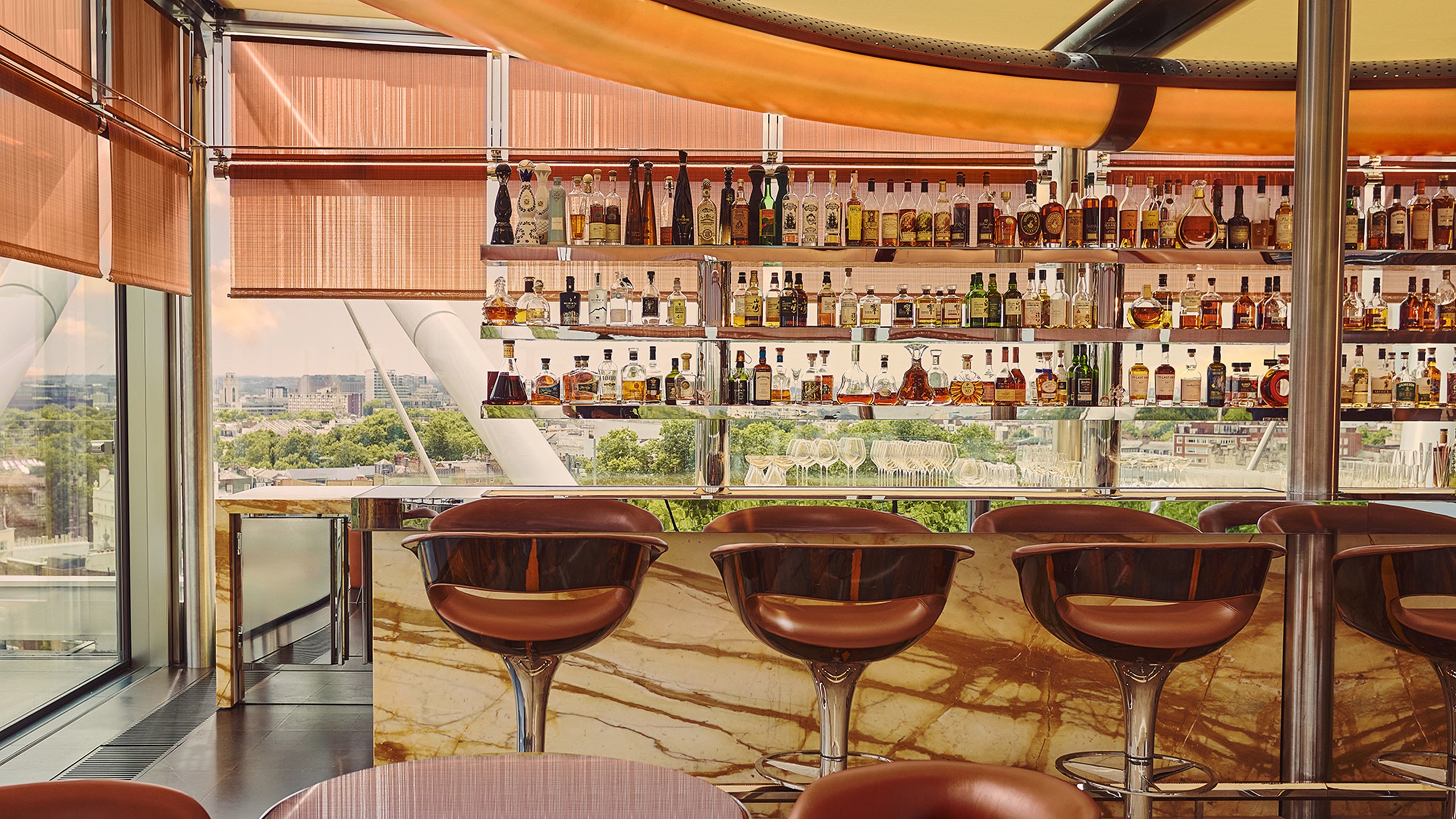 Marble bar with high leather stools and mirrored shelves stocked with spirits, set against floor-to-ceiling windows with city views.