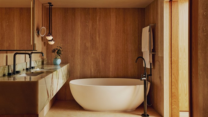 A luxurious bathroom with a freestanding white tub, earthy stone walls, and minimalist black fixtures for a modern touch.