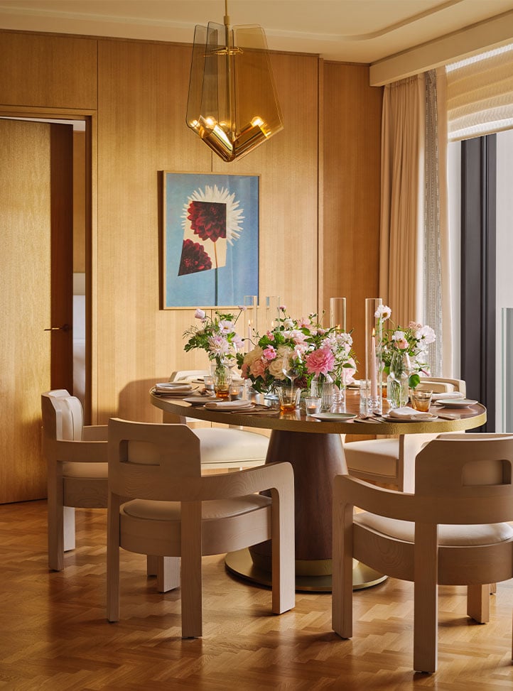 An elegant dining room with a round table set with delicate floral arrangements, set against a backdrop of warm wood paneling and soft lighting.