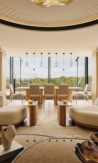 The Emory Penthouse, light elegant room with white sofas, dining table and chairs, contemporary downlighters and floor to ceiling windows with a view of Hyde Park in the background.