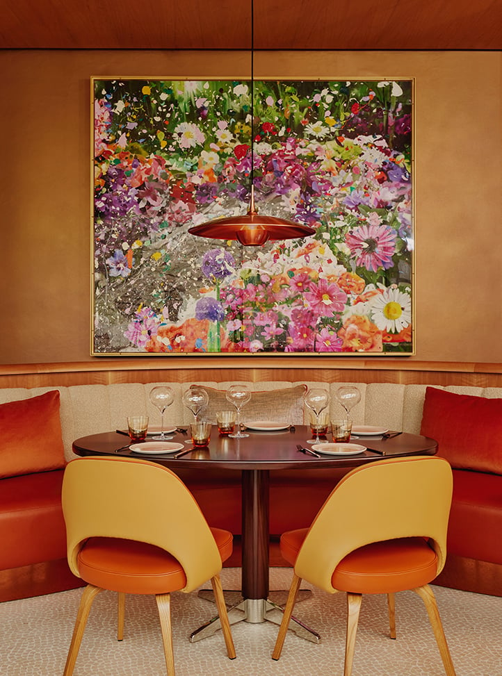 Two curved dining chairs sitting by a dining table with a statement piece of floral art on the wall
