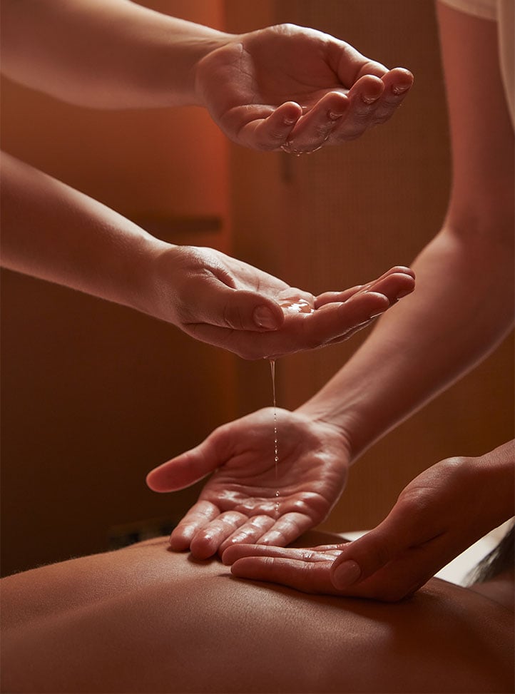 A close-up of a therapist’s hands delicately pouring warm oil into a client’s palms, capturing the essence of mindful relaxation and indulgence.