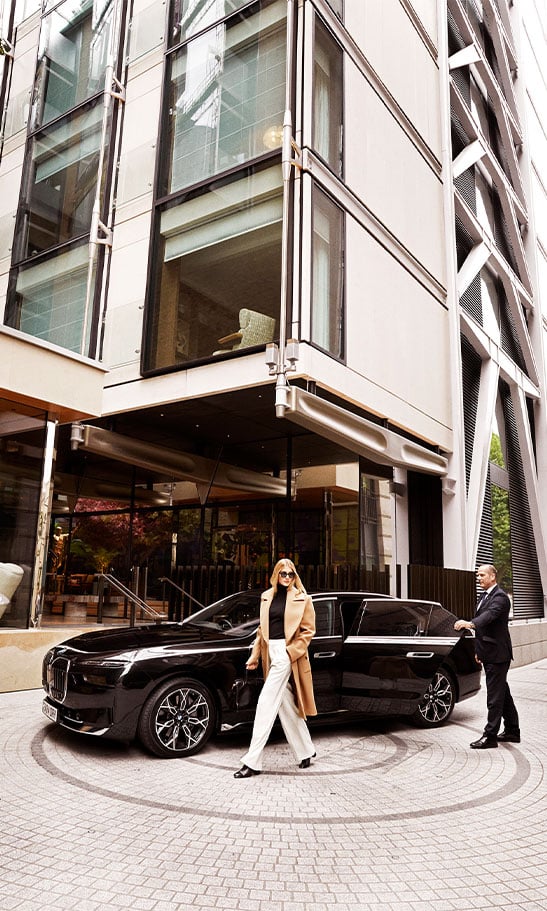 Elegant city arrival: A woman steps gracefully from a sleek black luxury car, framed by modern architectural glass and steel