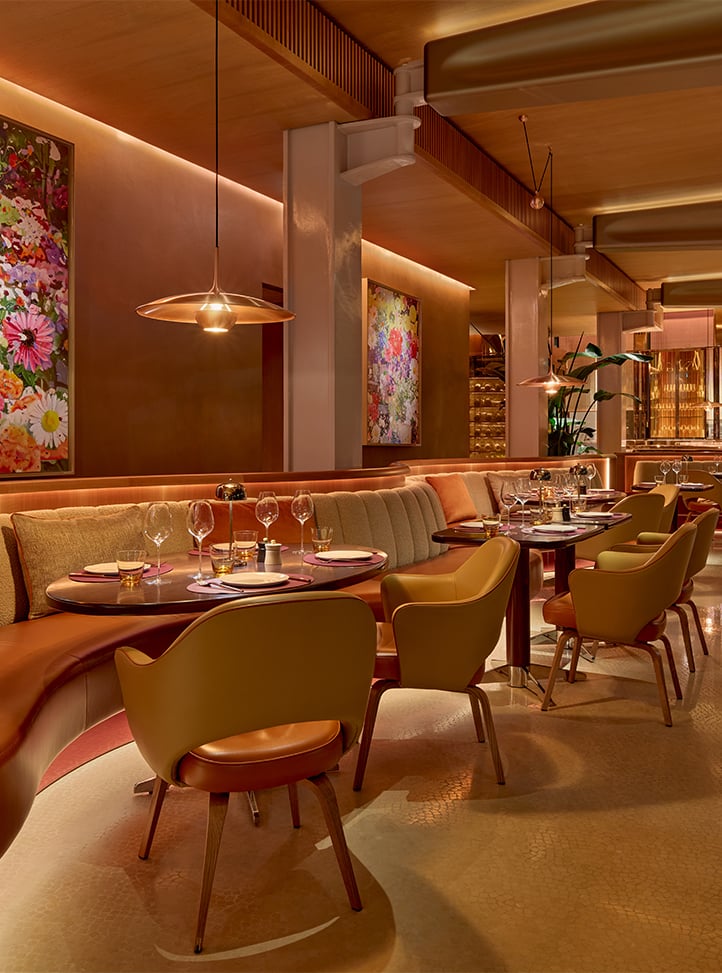 A beautifully lit dining area with plush banquettes, framed by vibrant artwork and a stylish bar in the background, creating a warm, welcoming environment for an elegant dining experience.