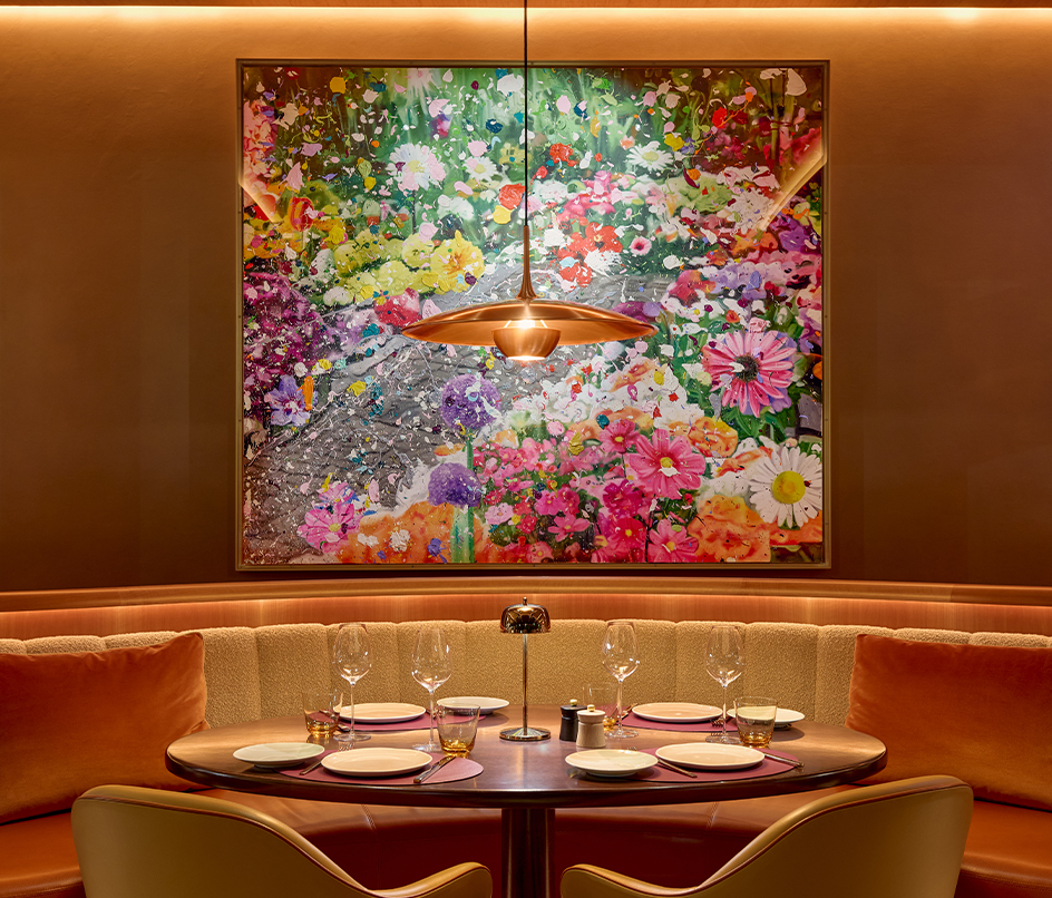 A cozy, elegantly set dining table with plush seating, adorned with soft lighting and framed by a vibrant floral artwork, creating a warm and inviting atmosphere.