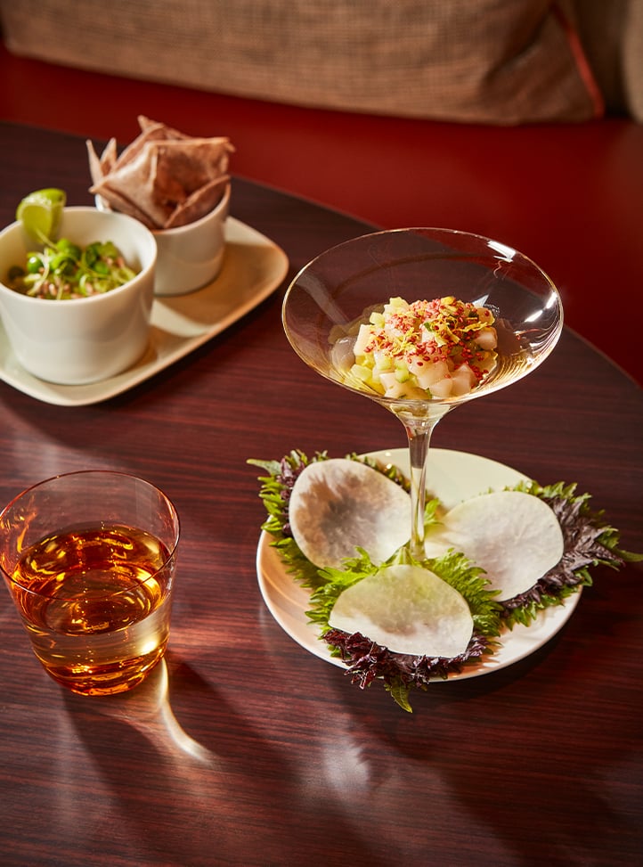 Aesthetic table set up with orkey sea scallop tartare in a coup, with a glass of water and green chickpea hummus in a bowl.