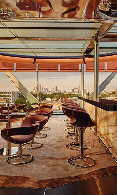View of Bar 33 with tables, chairs, the bar and stool tucked beneath. Outside the view is over London's urban landscape.