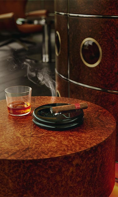 vA luxurious setup with a glass of amber whiskey and a lit cigar on a polished wood table.