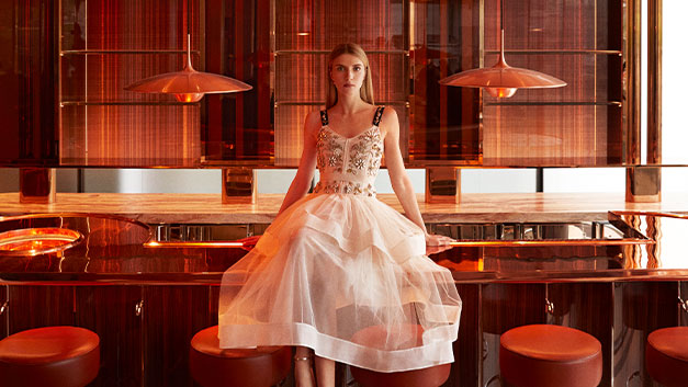 Model sat on The Emory bar wearing white dress with embellished bodice.