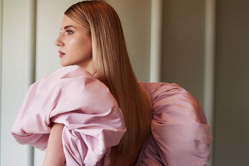 Model in pink dress with eccentric puffed sleeves in Emory Suite, standing at a side angle.