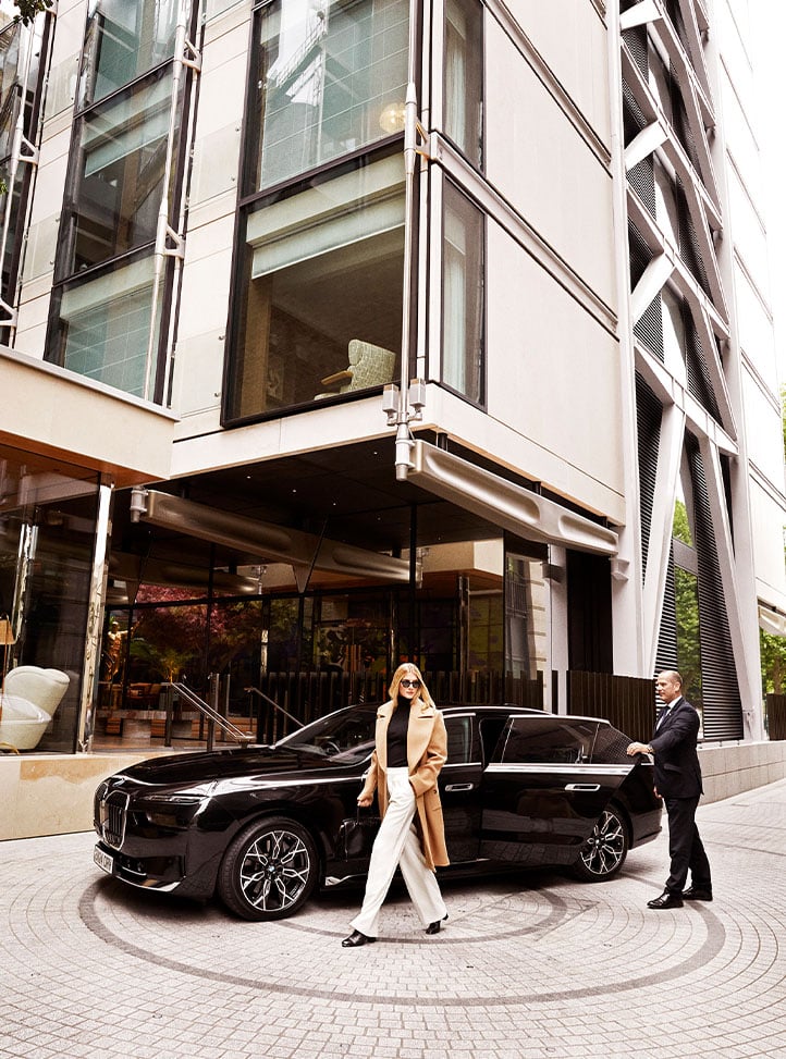 A luxury arrival at The Emory, as a guest steps out of a black BMW, greeted by a doorman against the hotel's striking modern exterior.