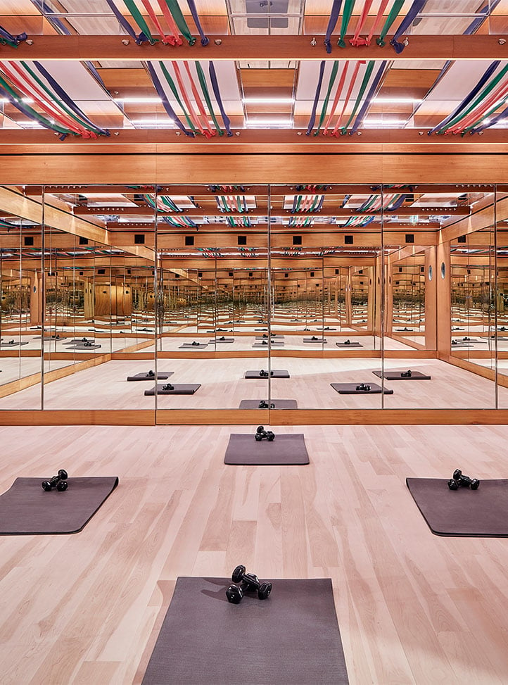 A beautifully designed fitness studio featuring wooden floors, mirrored walls, and resistance bands suspended from the ceiling, with workout mats and dumbbells neatly arranged.