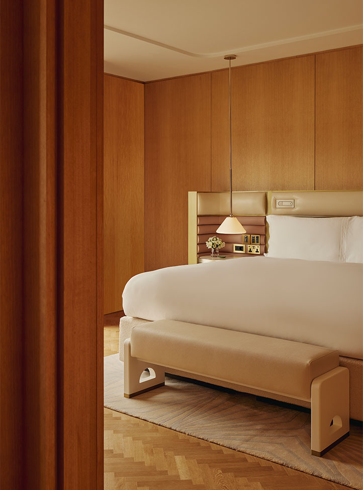 A tranquil bedroom with rich wood paneling, a plush white bed framed by a custom leather headboard with built-in lighting, and a sculptural pendant lamp, complemented by a contemporary upholstered bench.