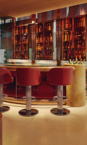 A sophisticated bar area with rich red seating and a warmly lit backdrop of fine spirits, creating an inviting atmosphere for a luxurious cocktail experienc