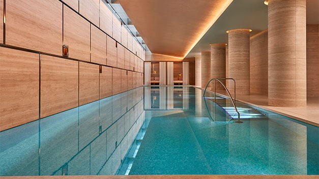 A serene indoor pool with tranquil lighting and sleek stone columns, creating a peaceful ambiance for relaxation and rejuvenation.