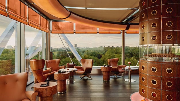 A refined cigar lounge featuring luxurious leather seating and warm wood accents, with floor-to-ceiling windows offering sweeping views of lush greenery.