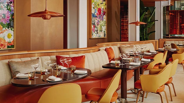 A chic dining area with plush seating in warm tones, adorned with colorful floral artwork, and elegantly set tables that invite a sophisticated dining experience.