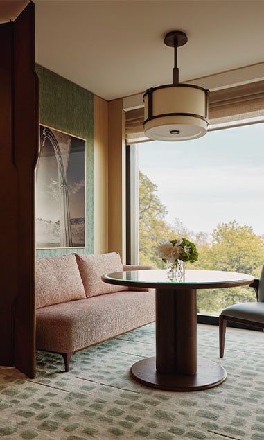 Park Junior Suite sitting area. A window sits in the background and a glass and a couch sits beside it. A circular wooden and glass table sits in front of the couch and a chair sits beside it.