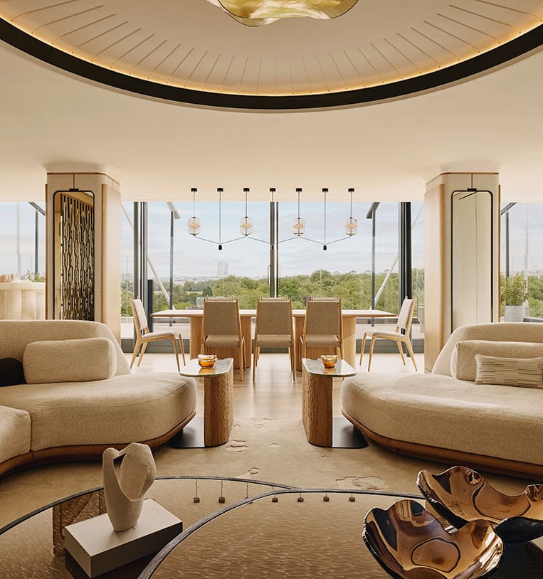 The Penthouse at The Emory. A large window looks over Hyde Park and the living room in the foreground is full of cream soft furnishings.